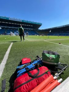 Automated external defibrillator (AED), first aid kit, oxygen cylinder bag, mixed analgesic gas cylinder bag, carry chair & folding stretcher located in the dugouts next to the grass football playing surface within a licensed sports ground (stadium)